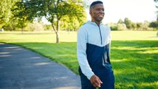 A smiling man walks outside in a sunny park.