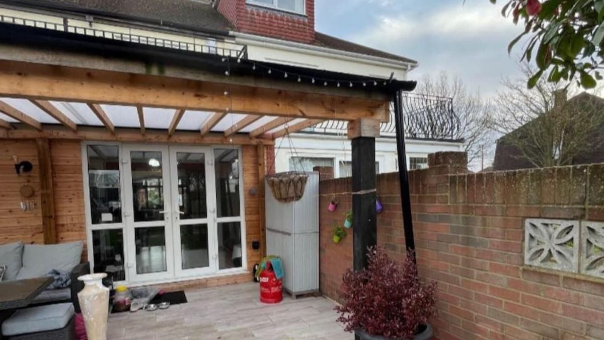 A canopy attached to a brick house with an outdoor seating area beneath