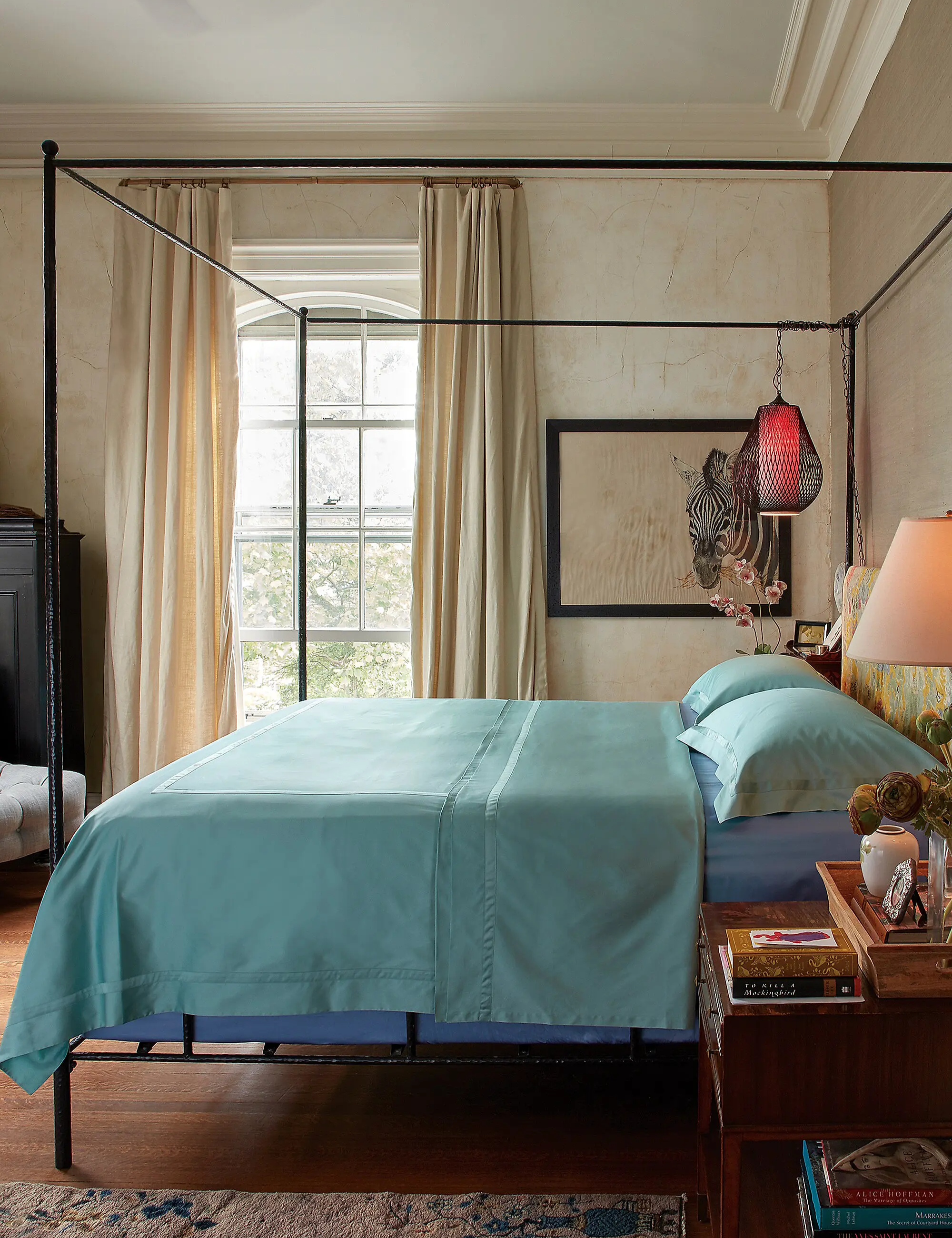 Aquamarine bed sheets styled atop of an iron four-poster bed inside of an opulent bedroom