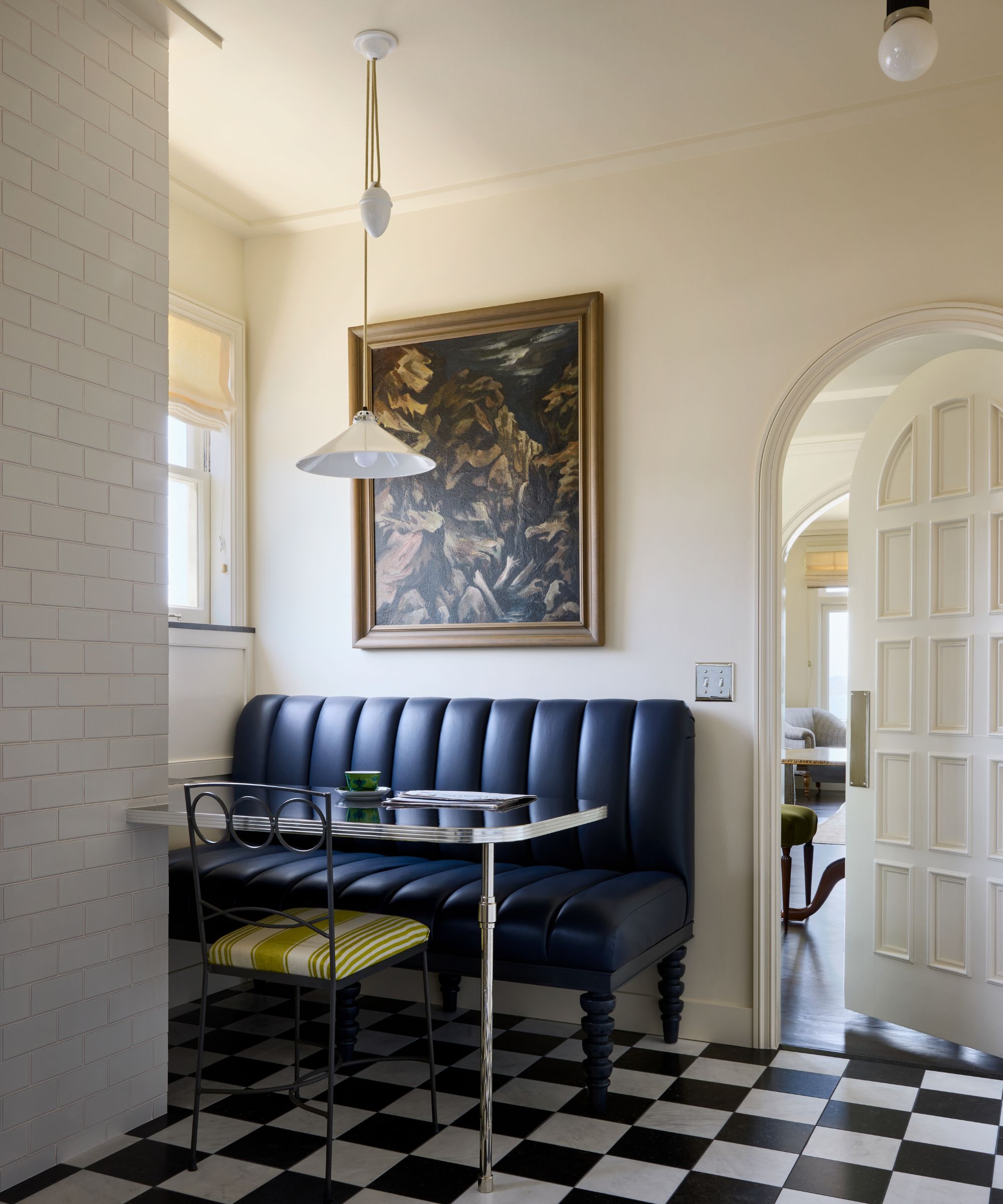 a soft off white kitchen with arched door, black and white checkerboard tiled floor and a new york style bistro dining nook