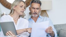 Older couple holding paperwork and a tablet discussing finances 