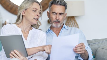 Older couple holding paperwork and a tablet discussing finances 