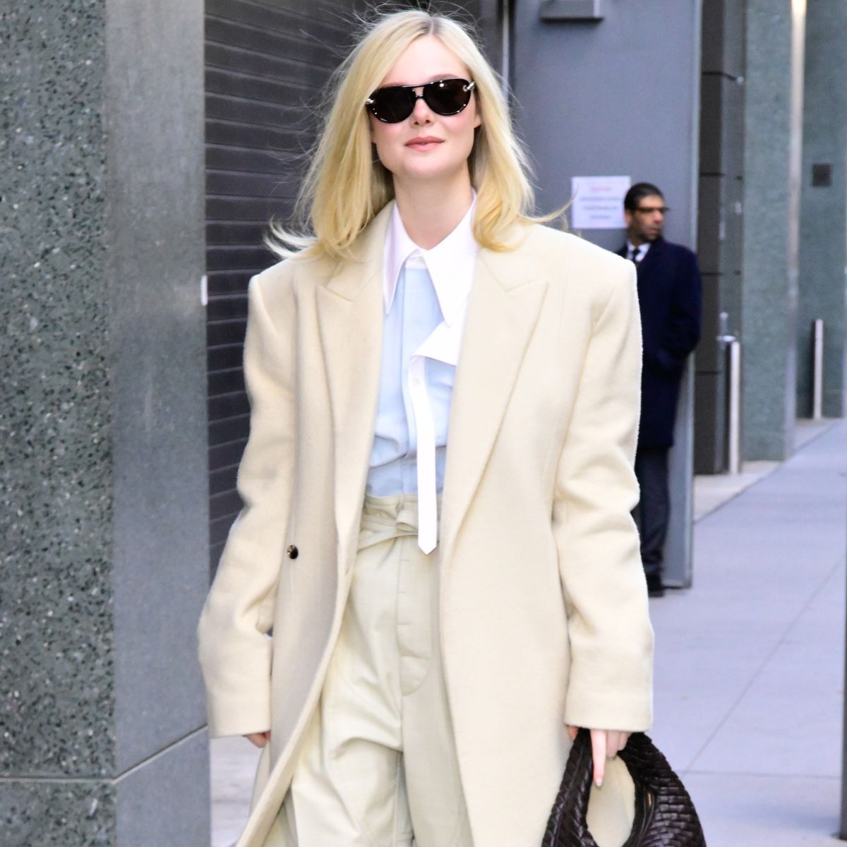 elle fanning wears an off-white cream coat and trousers and blue shirt