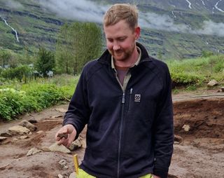 A man stands outside holding the tiny carved toy in his hand