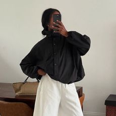 a woman wearing a black funnel neck jacket with white pants