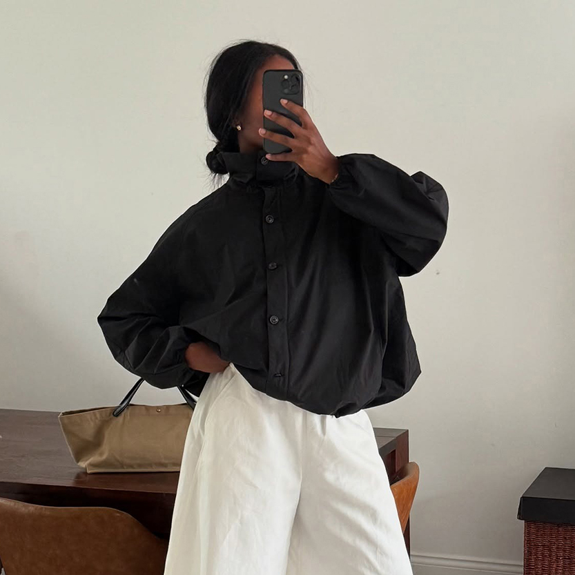 a woman wearing a black funnel neck jacket with white pants