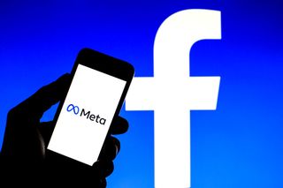A smartphone showing the Meta company logo in front of a large Facebook logo