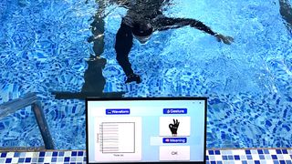 A diver in a swimming pool makes a hand gesture, which is translated into words on a screen.