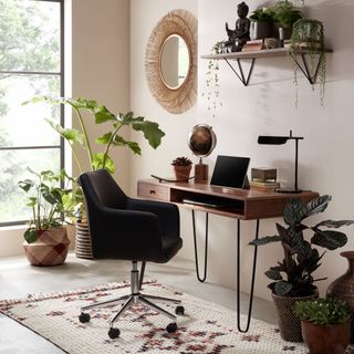 Earthy home office with mid-century desk, iron legs, ergonomic fabric chair, berber style rug and rattan mirror with decorative houseplants