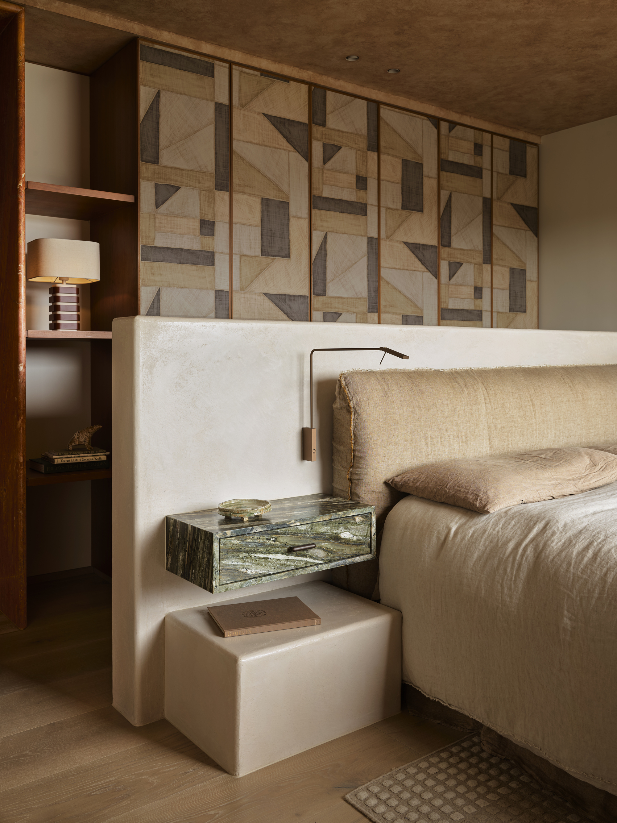 A bedroom with a geometric patterned wall, a large built-in headboard and a bed styled with neutral bedding