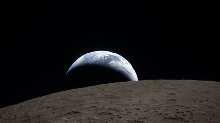 Earthset captured through the Orion spacecraft window at 6:41 p.m. EDT, April 6, 2026, during the Artemis II crew’s flyby of the Moon. A muted blue Earth with bright white clouds sets behind the cratered lunar surface. The dark portion of Earth is experiencing nighttime. On Earth’s day side, swirling clouds are visible over the Australia and Oceania region.