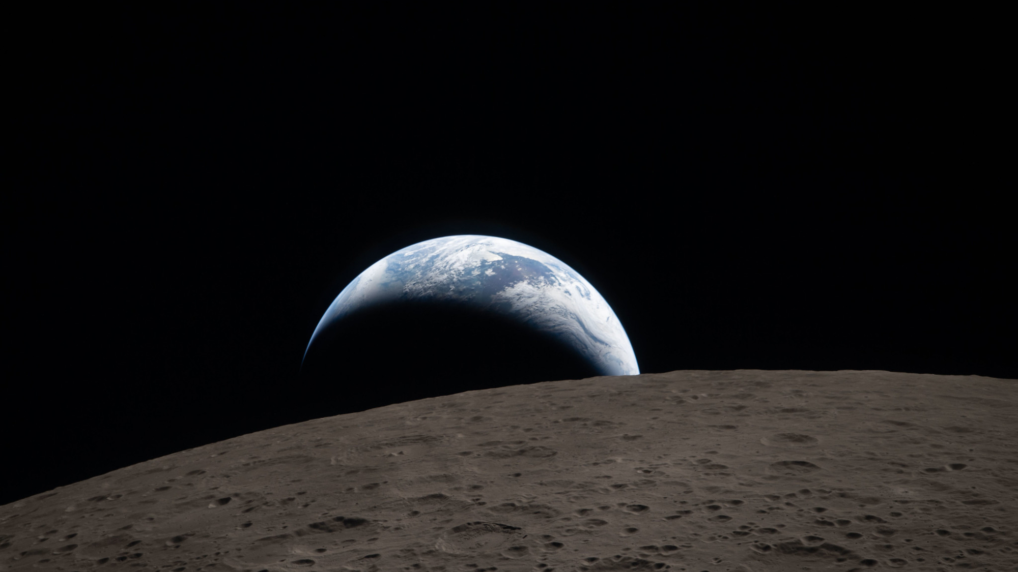 Earthset captured through the Orion spacecraft window at 6:41 p.m. EDT, April 6, 2026, during the Artemis II crew&amp;rsquo;s flyby of the Moon. A muted blue Earth with bright white clouds sets behind the cratered lunar surface. The dark portion of Earth is experiencing nighttime. On Earth&amp;rsquo;s day side, swirling clouds are visible over the Australia and Oceania region.