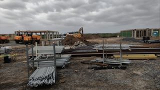 Piles of pipes and construction materials on a bare plot of land.