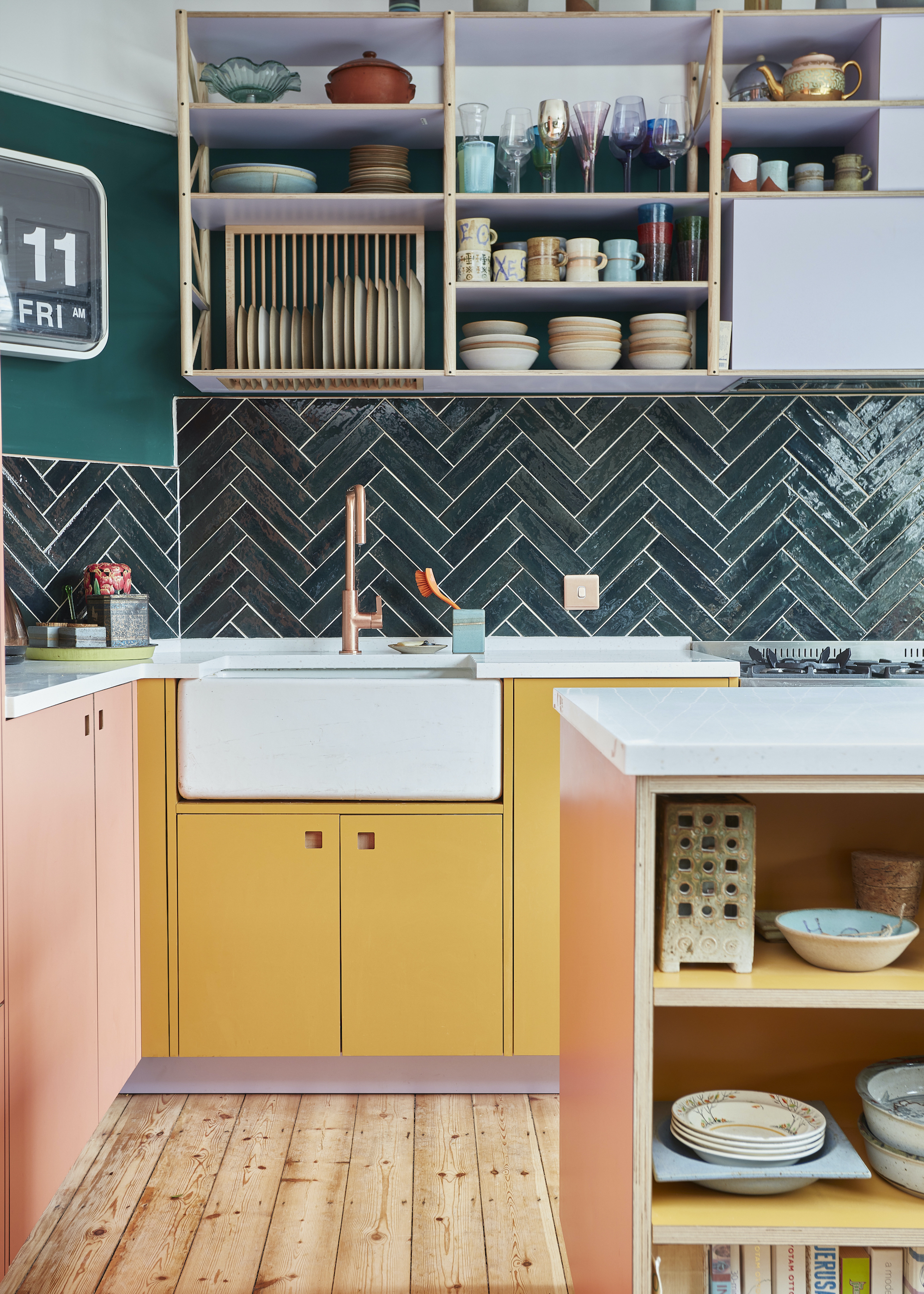 A kitchen with pink and yellow cupboards as well as open shelving on both the kitchen island and above the kitchen sink