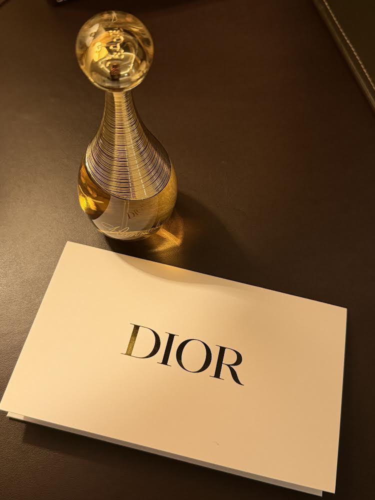 a gold perfume bottle next to a white piece of paper with "dior" printed on it