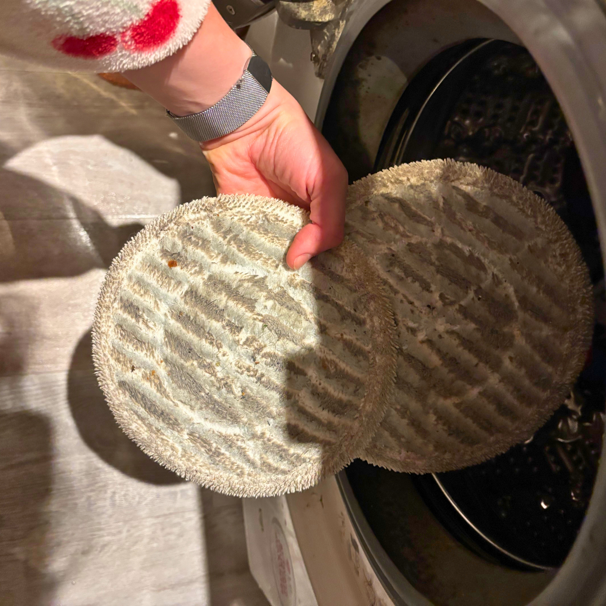 Hand holding dirty dual mop pads after use, in front of open washing machine door