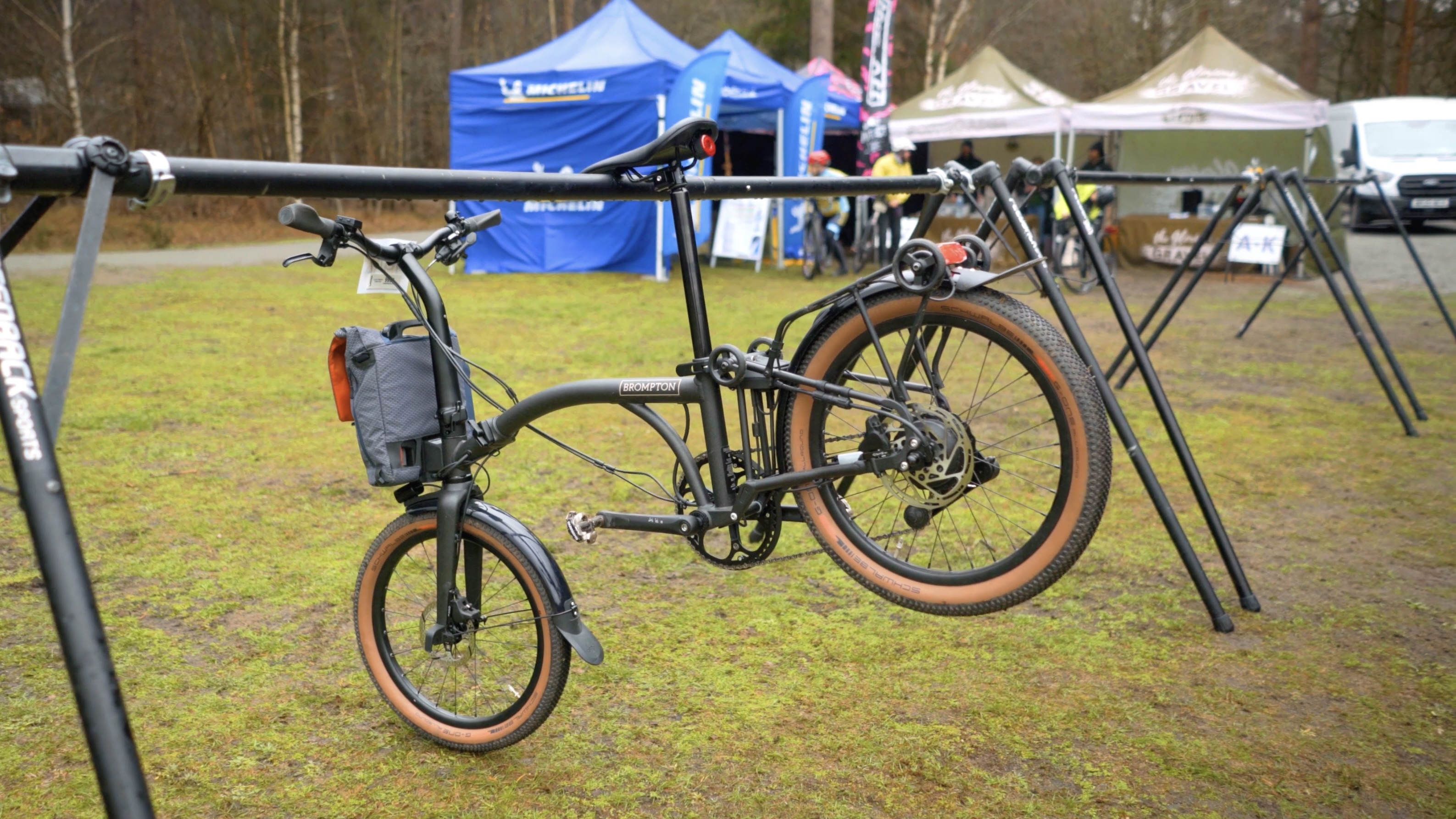 An orange Brompton covered in mud on a light gravel track