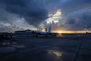 a large aircraft on a tarmac under dark thunderclouds