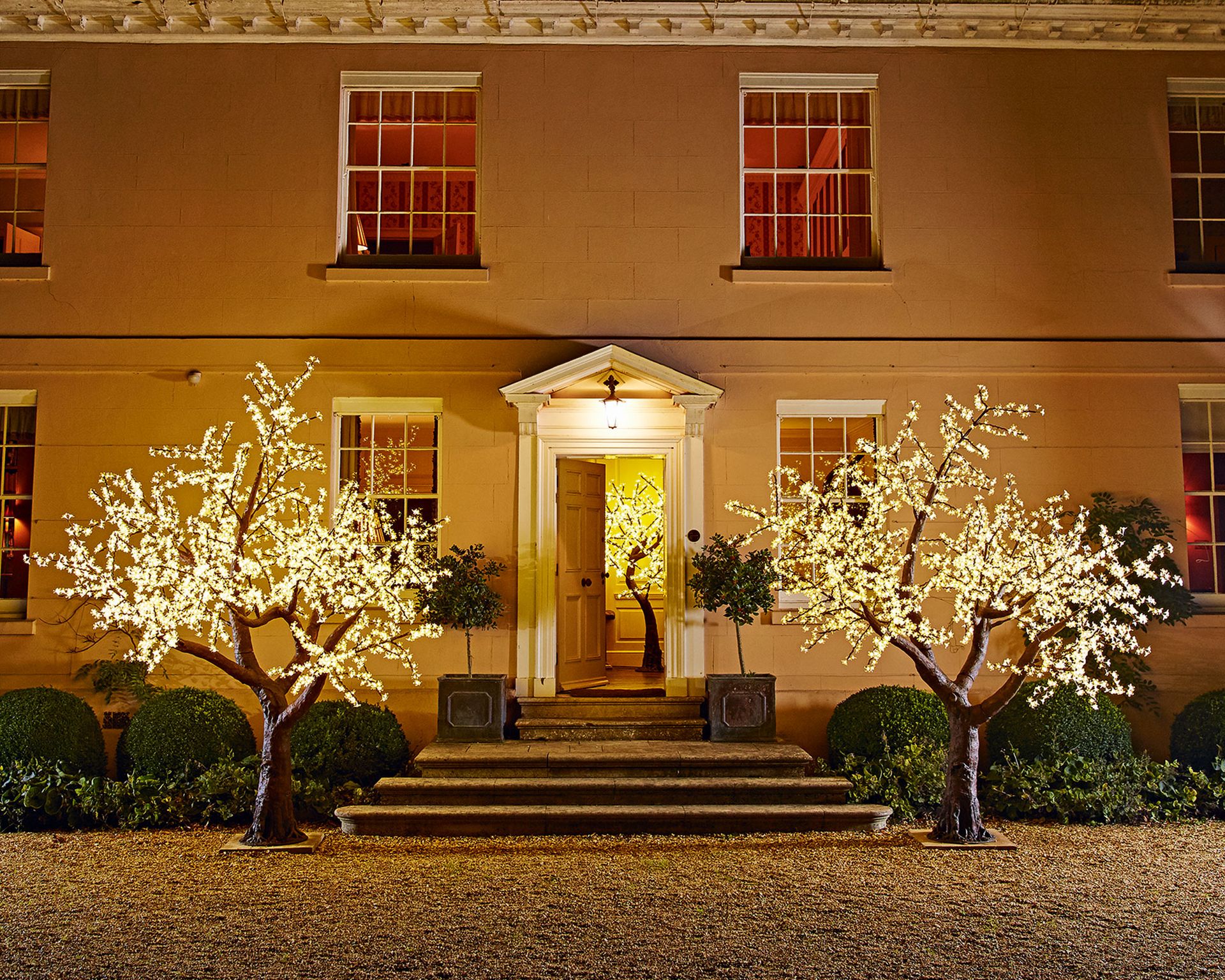 An example of outdoor lighting ideas showing a porch area with lit-up symmetrical trees