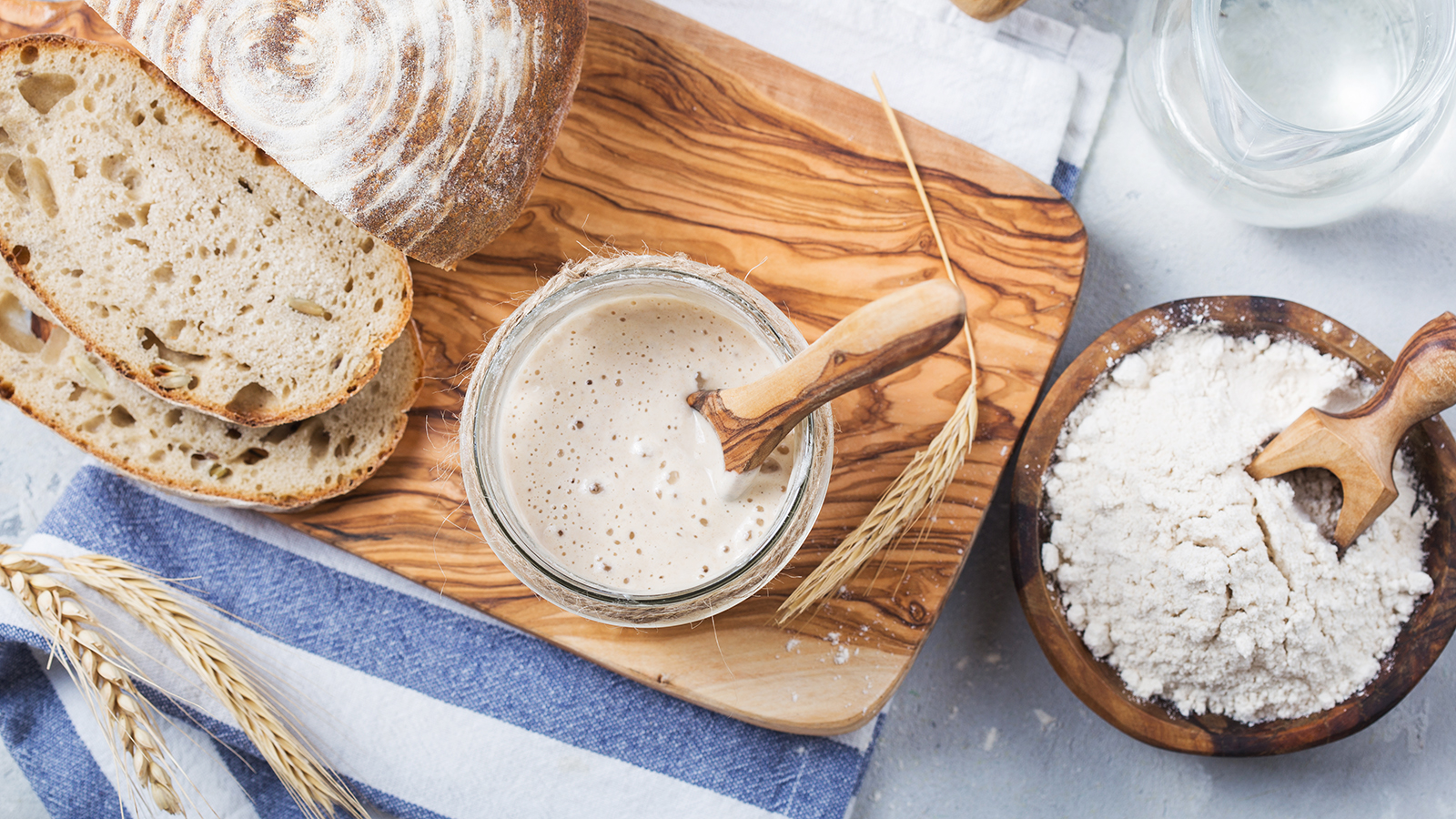 Sourdough starter next to loaf of bread and flour
