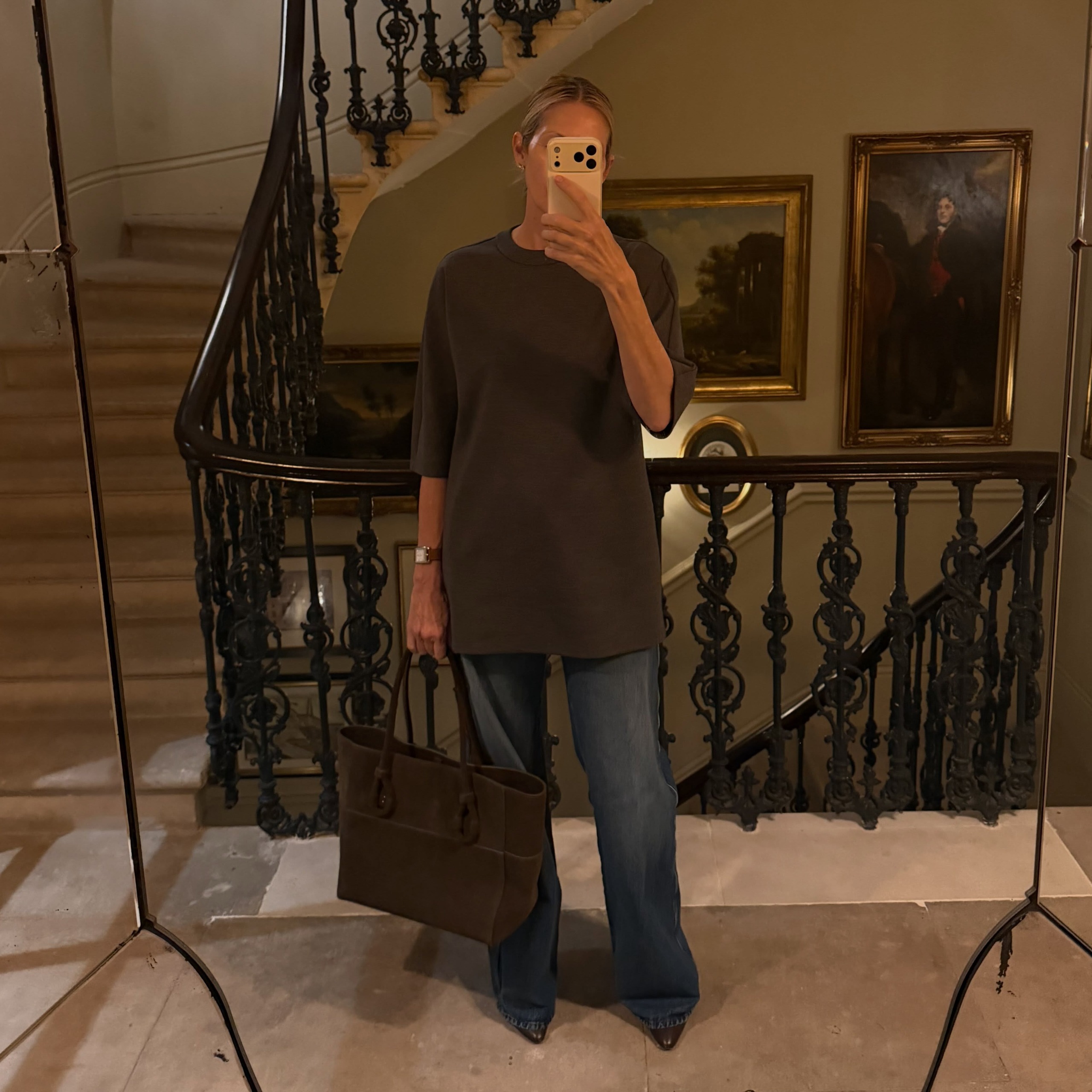 Kelly Rutherford takes a mirror selfie wearing a short-sleeve knit with dark wash jeans and a black suede bag.