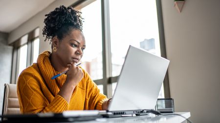 A woman looks at her laptop while sitting at her desk.