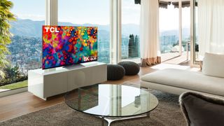 The TCL 6-Series 8K TV in a living room on a TV stand.