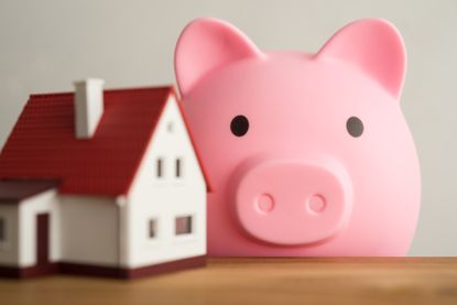 Home on a wooden table with a cute pink piggy bank and a white wall background.