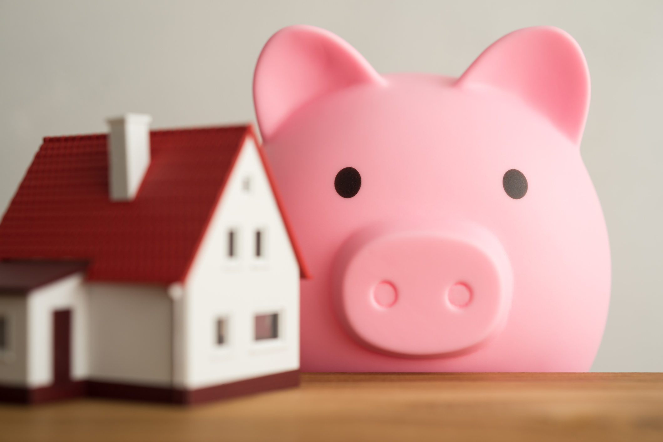 Home on a wooden table with a cute pink piggy bank and a white wall background.
