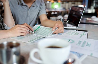 Close-up shot of unrecognizable young family sitting at cafe table and reading life insurance brochure, blurred background