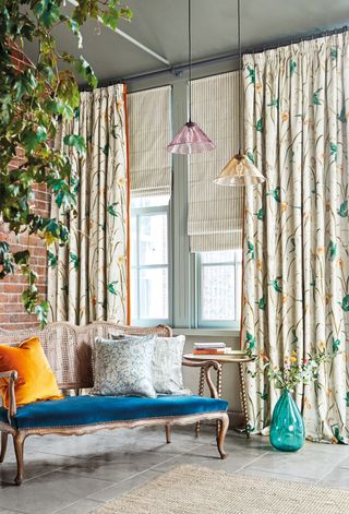 Color pop scheme with stylized floral floor length drapes, and cane and velvet sofa with blue seat, and colored glass hanging pendant lights.