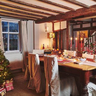 Christmas tree and dining table with festive touches candles lit in cottage with beams and staircase behind