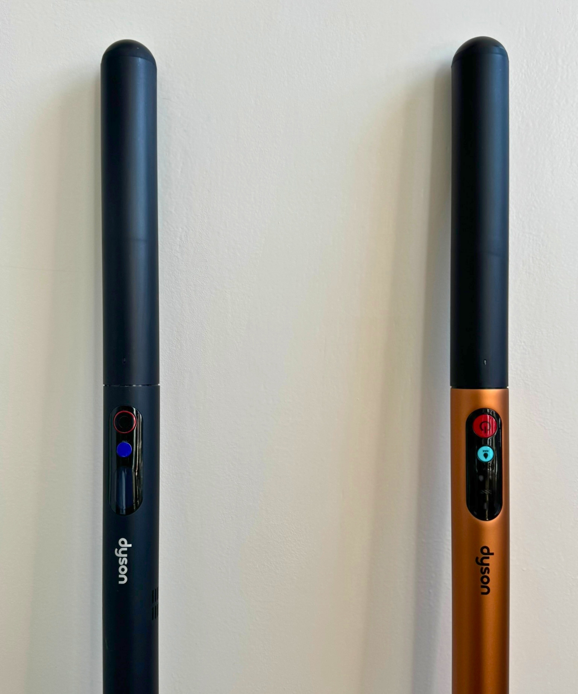 Handles and power buttons of the Dyson PencilVac and Dyson PencilWash against white wall.