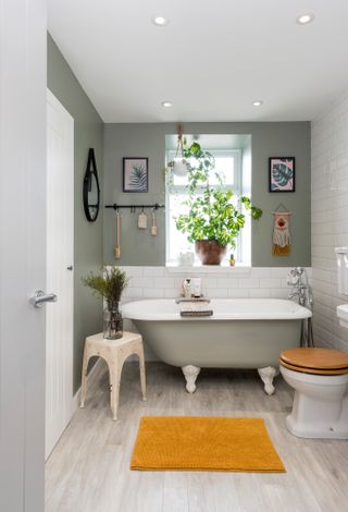 A neutral green bathroom with freestanding roll-top bath and wood effect flooring