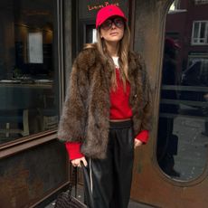 Woman in a red cap, red sweater, faux-fur coat and black pants