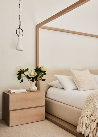 A bedroom with a side table, a vase of flowers and a pendant light