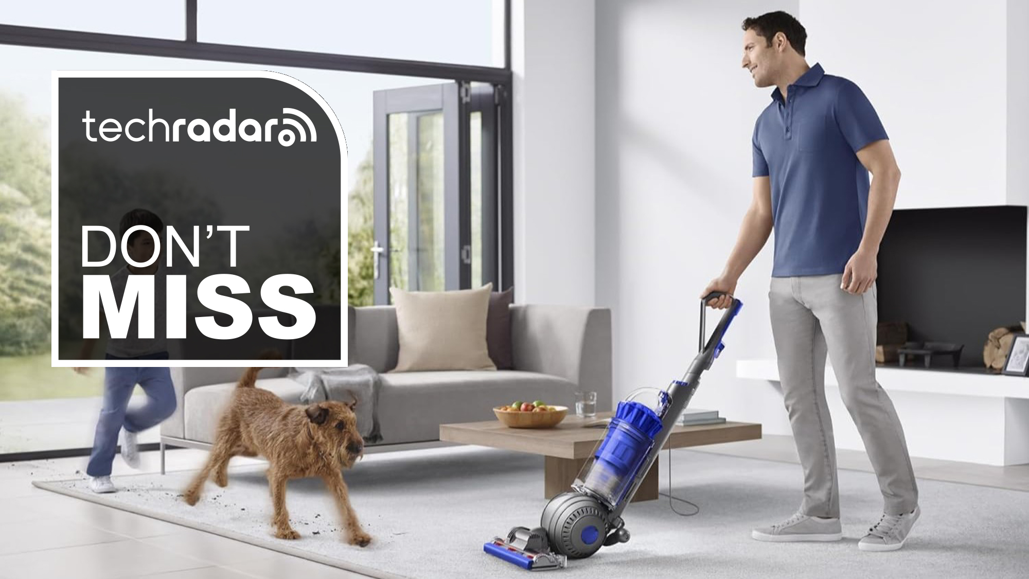 man using Dyson Ball Animal Total Clean vacuum with dog in living room