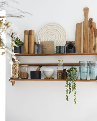 wooden shelving on a white wall holding plants, jars and other kitchen accessories