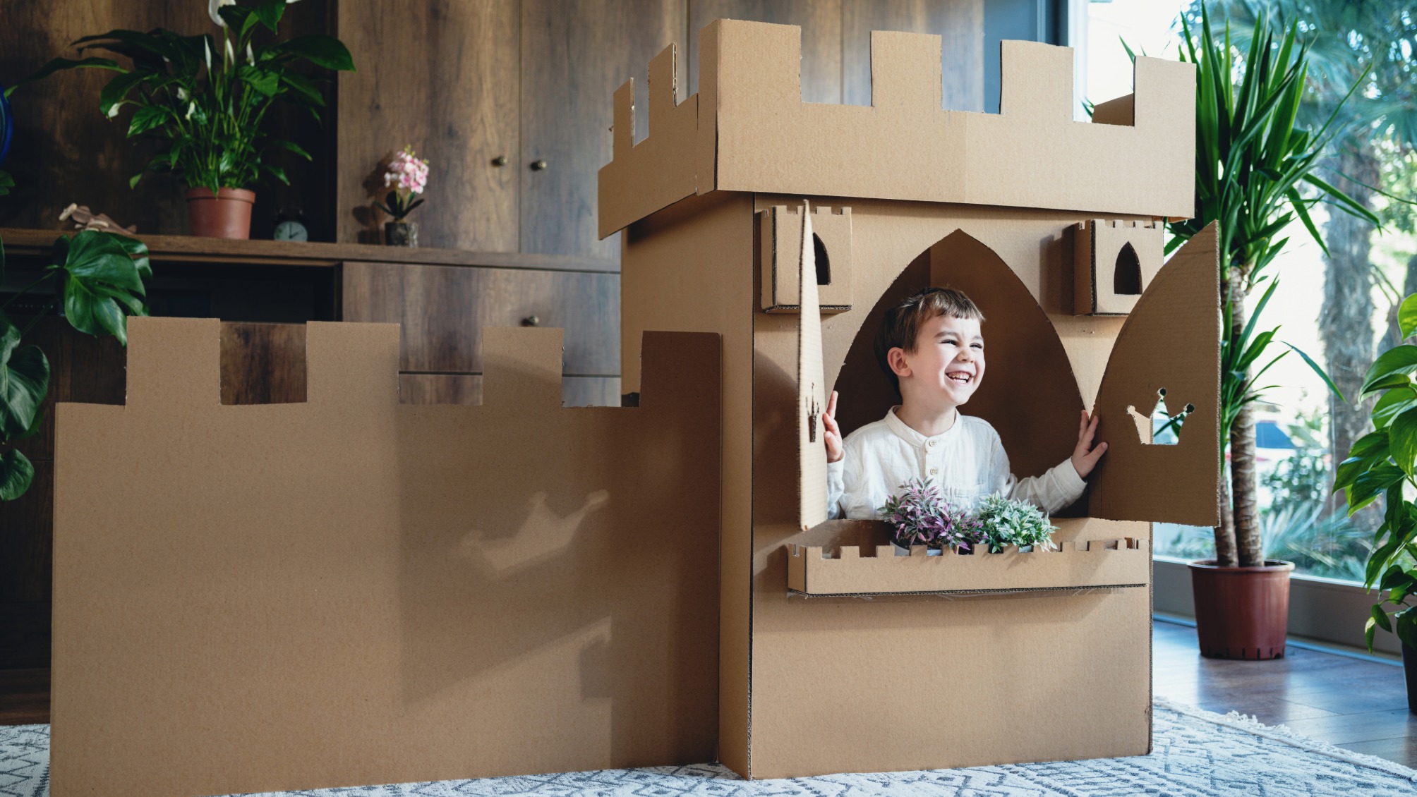 Young Boy Playing Role Play At Home With Castle Made Of Cardboard