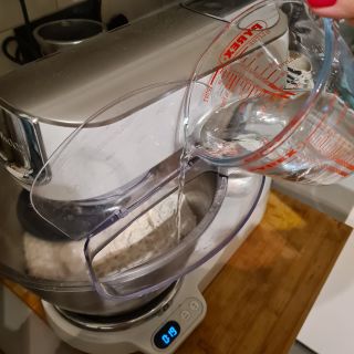 Kenwood Titanium Chef Baker containing bread dough and adding water from pyrex jug