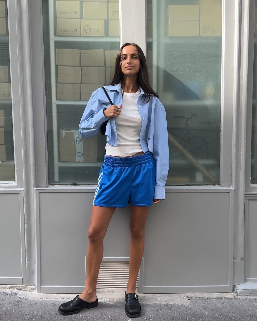 A woman wearing blue athletic shorts, a white tee, and cropped button-up.