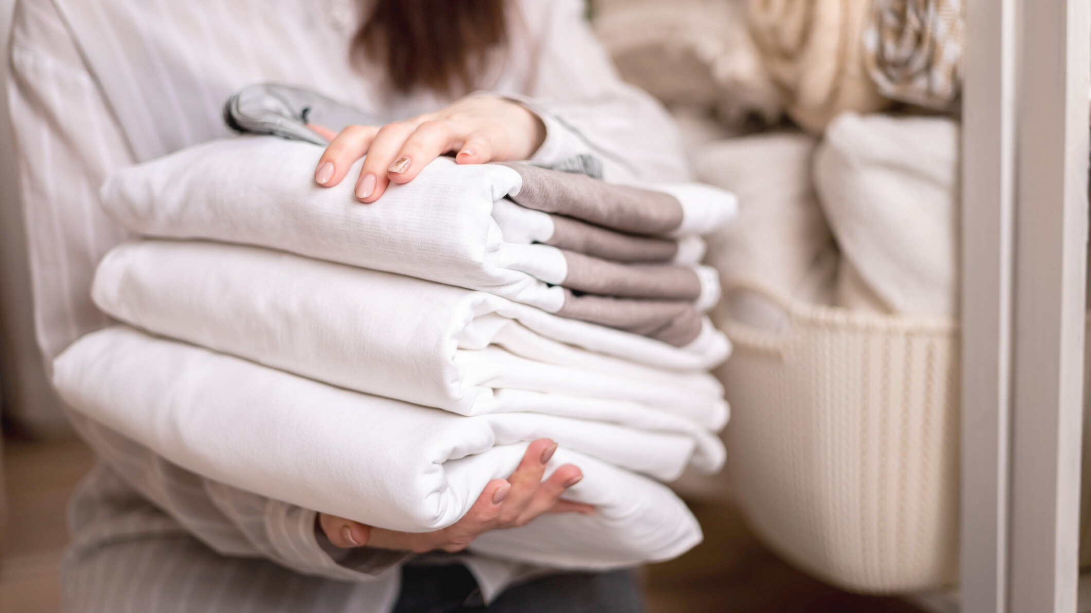 Woman holding a stack of washed and folded white bedding in hand