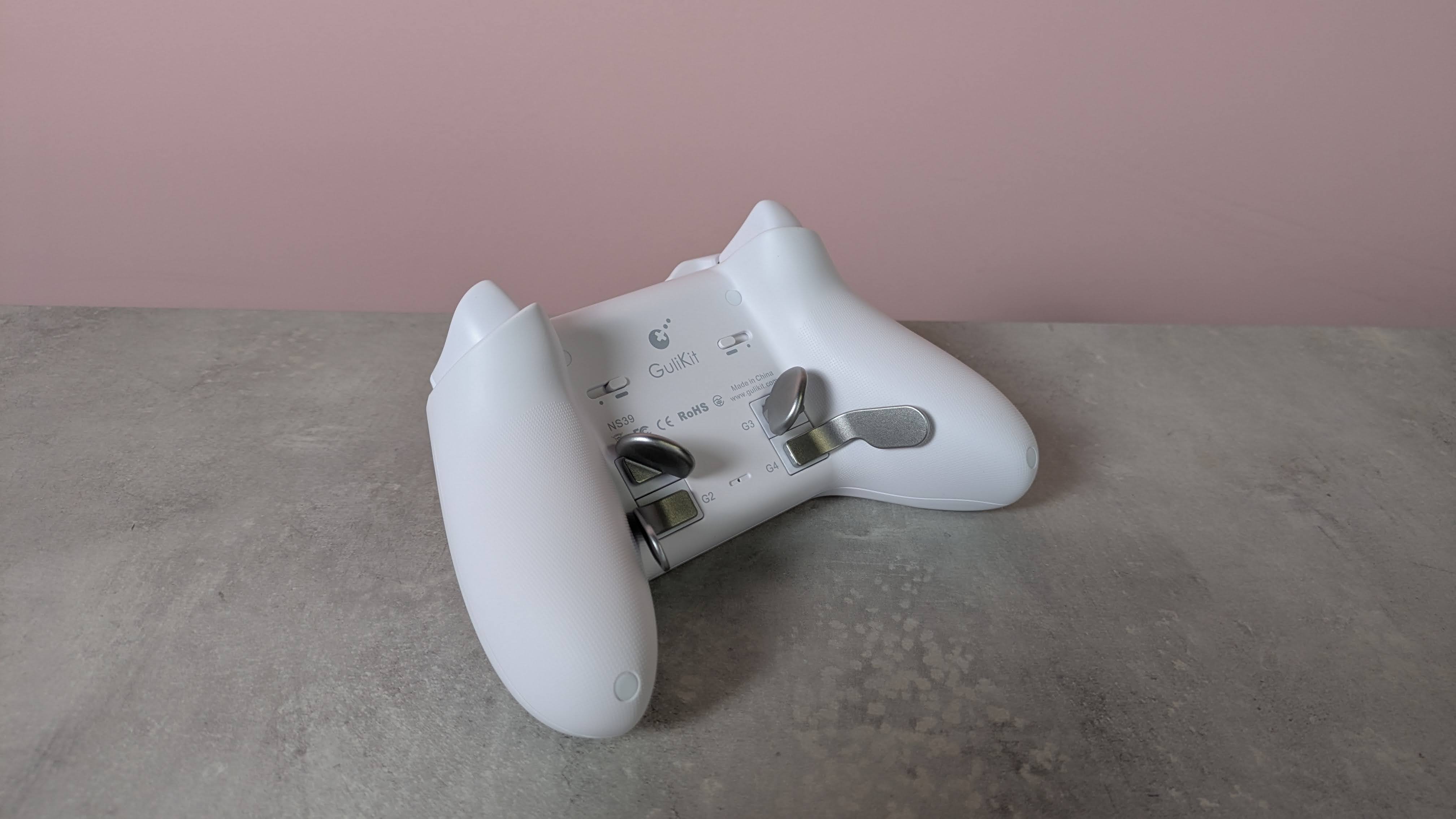 Back of GuliKit KK3 Max with back button levers attached, on a desk with pink wall in background