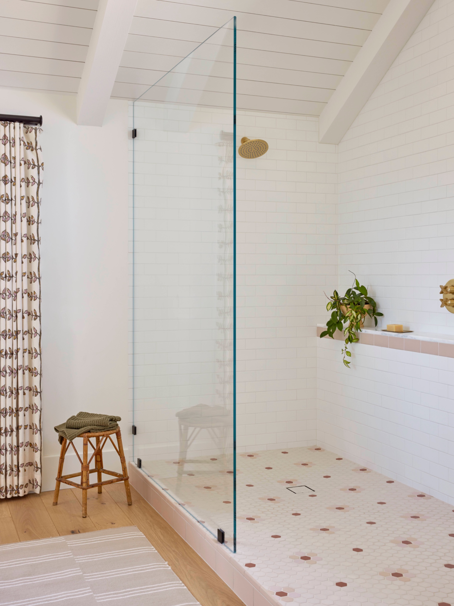 Glass shower enclosure with white subway-tiled walls, pink trim, brass fixtures and a hexagonal mosaic floor dotted with pink and terracotta flowers.