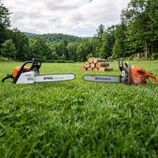 Two chainsaws facing each other on a grassy lawn with logs in the background