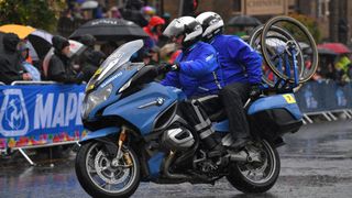 A motorbike carrying neutral support wheels rides through the rain