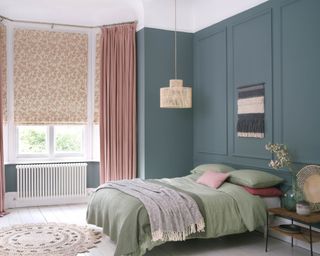 Bedroom with moody blue painted wall panels, and bay window with contrast blinds in blush tones.