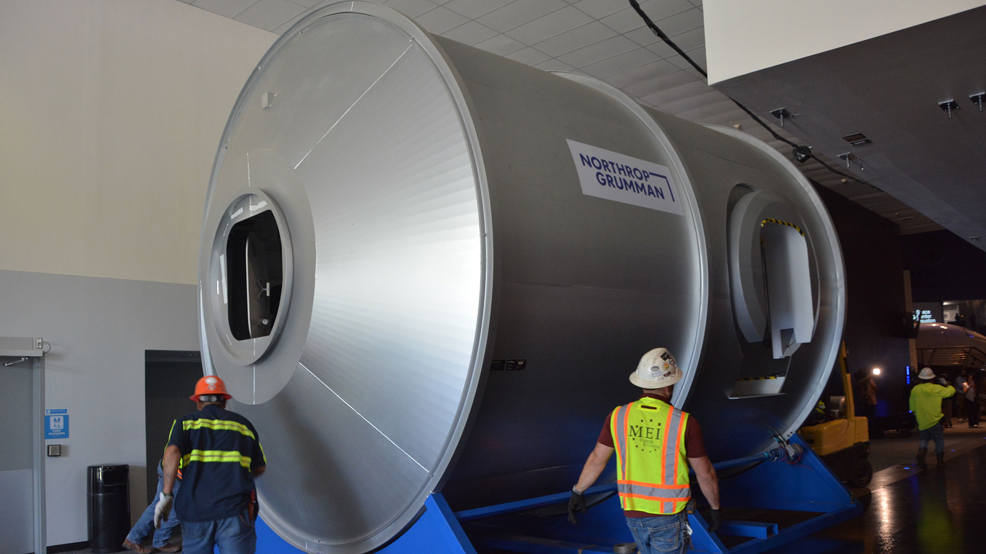 closeup view of a large silver cylindrical structure, with several men in hard hats around it