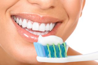A woman holds a toothbrush, full of toothpaste, near her mouth. 
