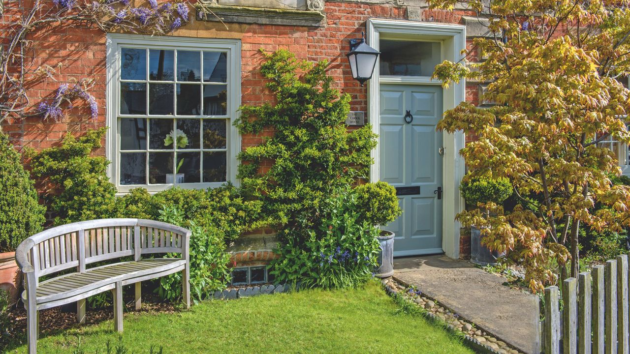 Front garden with wall-climbing plants, ornamental tree, garden path, small lawn area and bench